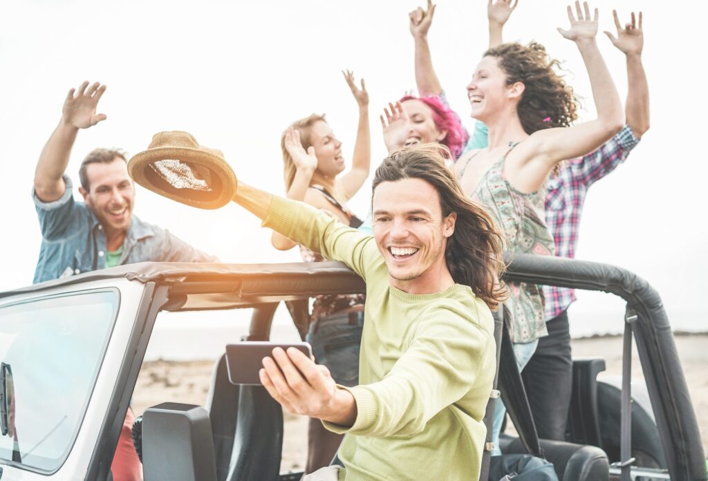 Trendy happy friends taking selfie with smartphone in desert on convertible jeep car